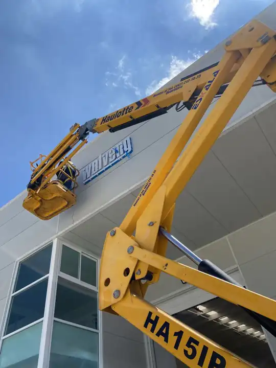 Grúa articulada instalando letras en fachada